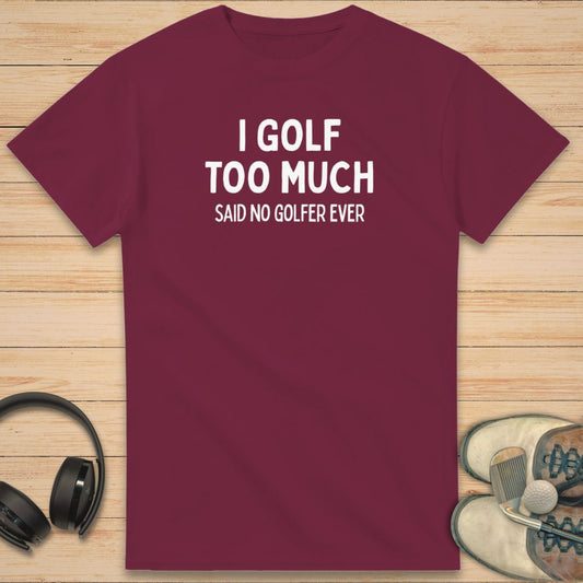 Golf Too Much T-Shirt in Maroon on a light wooden floor lying next to headphones and golf shoes.