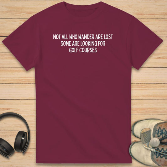 Golf Courses T-Shirt in Maroon on a light wooden floor lying next to headphones and golf shoes.