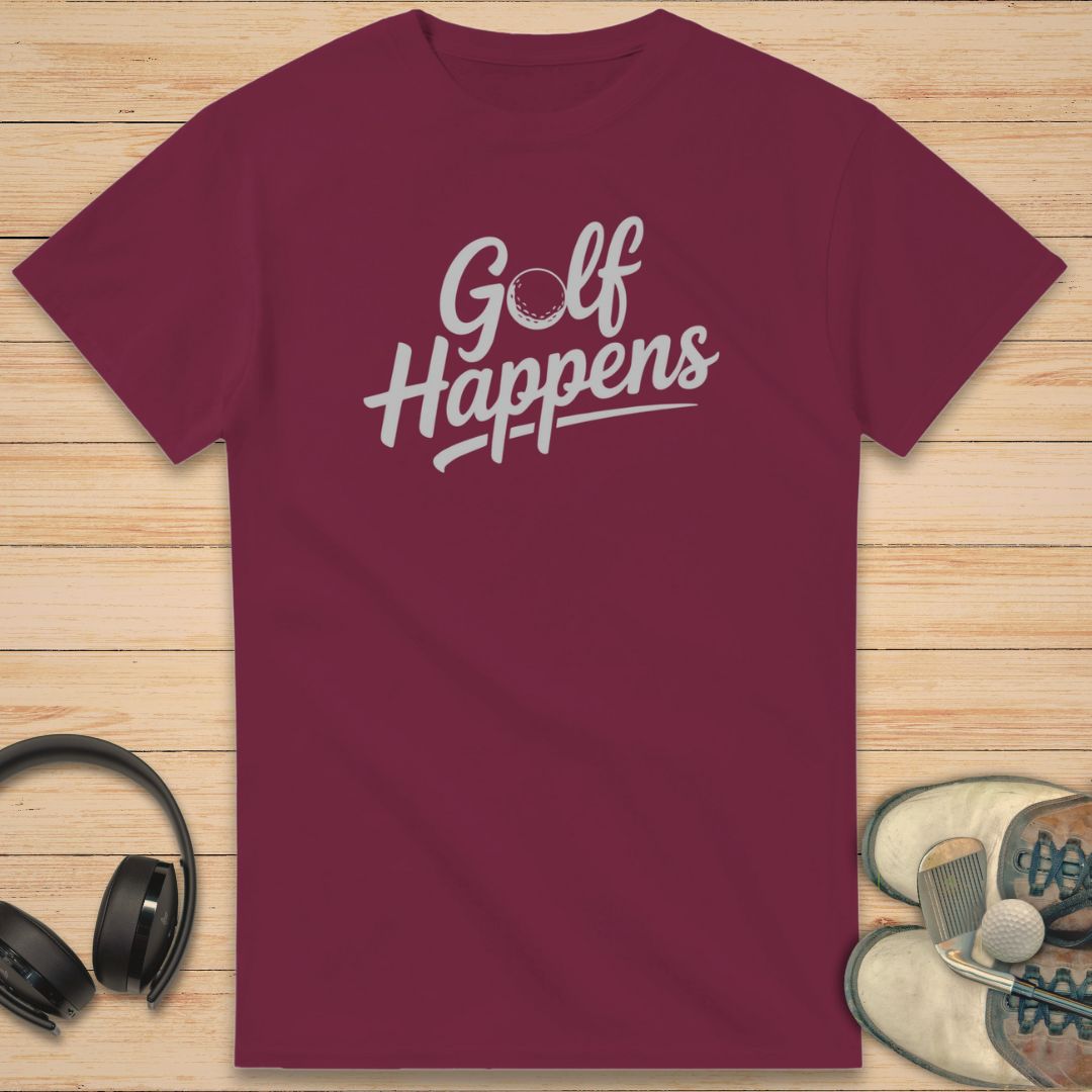 Golf Happens T-Shirt in Maroon on a light wooden floor lying next to headphones and golf shoes.