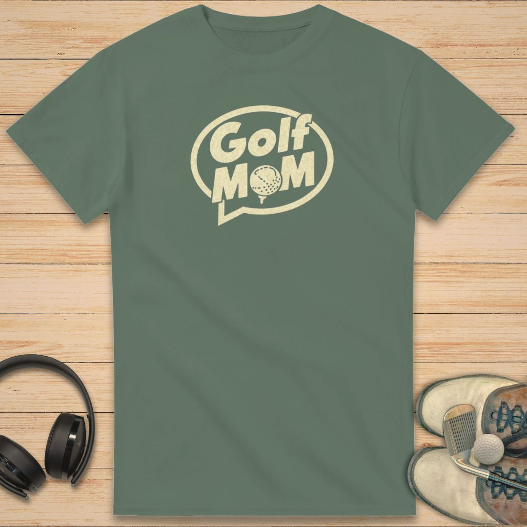 Golf Mom T-Shirt in Military Green on a light wooden floor lying next to headphones and golf shoes.