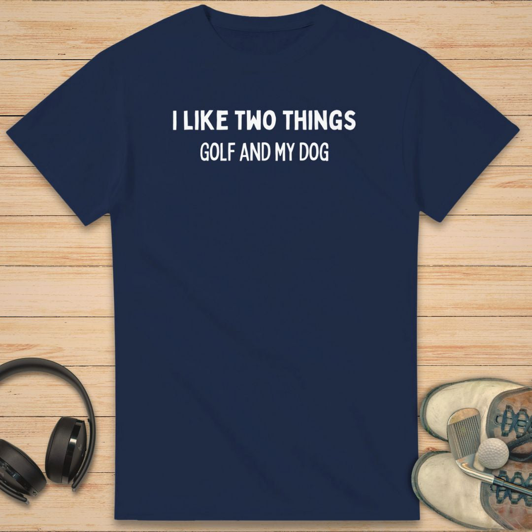 Two Things T-Shirt in Navy on a light wooden floor lying next to headphones and golf shoes.