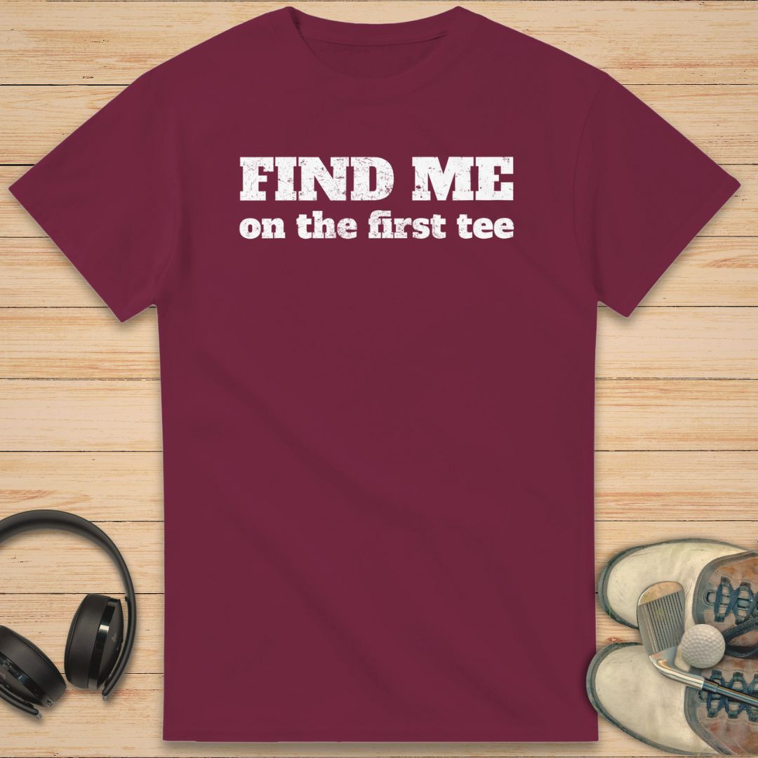 Find Me T-Shirt in Maroon on a light wooden floor lying next to headphones and golf shoes.