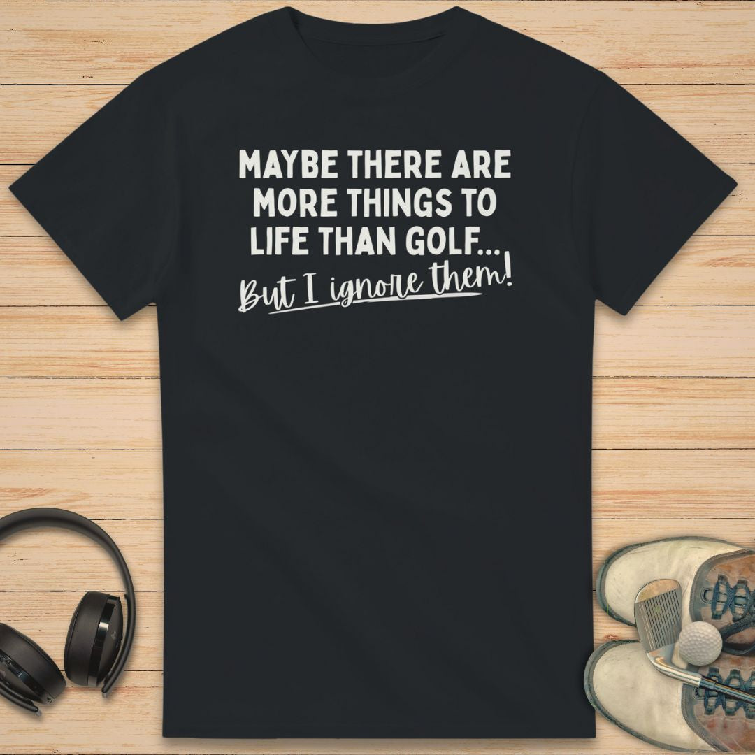 More Things T-Shirt in on a light wooden floor lying next to headphones and golf shoes.