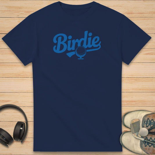 Birdie T-Shirt in Navy on a light wooden floor lying next to headphones and golf shoes.