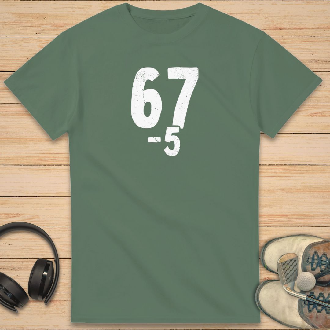 67 5 Under T-Shirt in Military Green on a light wooden floor lying next to headphones and golf shoes.