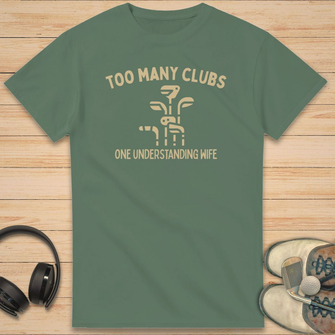 Understanding Wife T-Shirt in Military Green on a light wooden floor lying next to headphones and golf shoes.