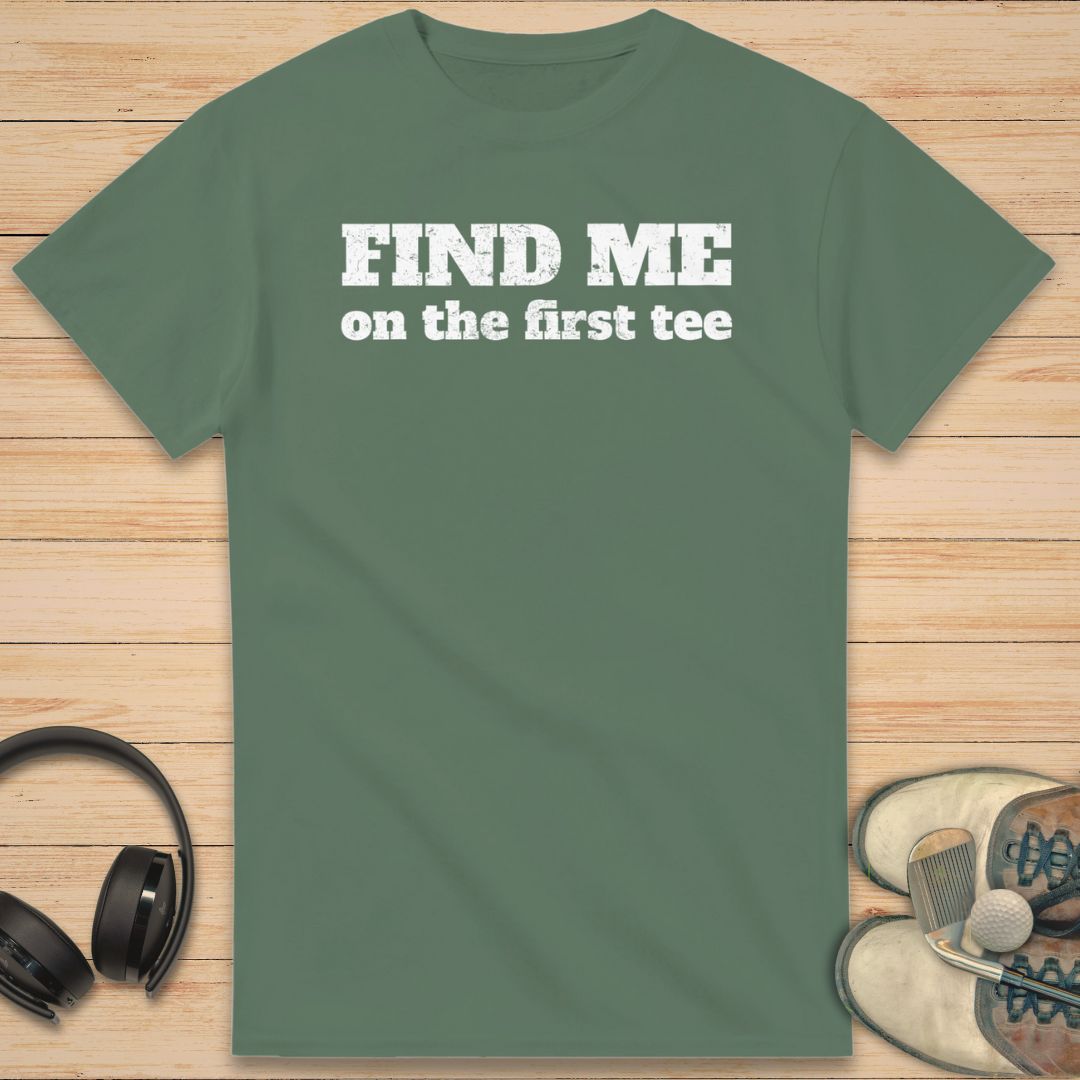 Find Me T-Shirt in Military Green on a light wooden floor lying next to headphones and golf shoes.