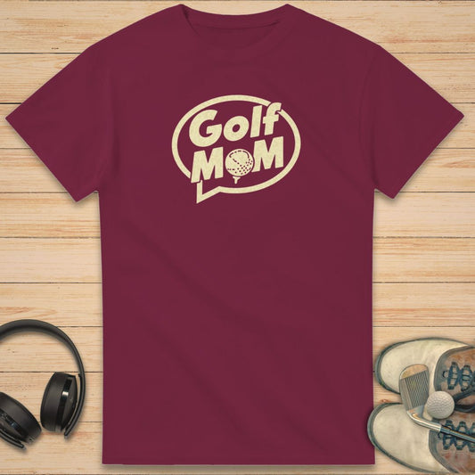 Golf Mom T-Shirt in Maroon on a light wooden floor lying next to headphones and golf shoes.