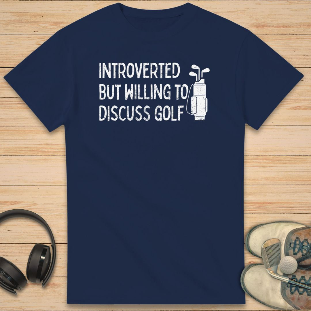 Introverted T-Shirt in Navy on a light wooden floor lying next to headphones and golf shoes.