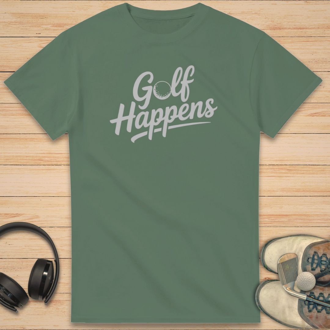 Golf Happens T-Shirt in Military Green on a light wooden floor lying next to headphones and golf shoes.