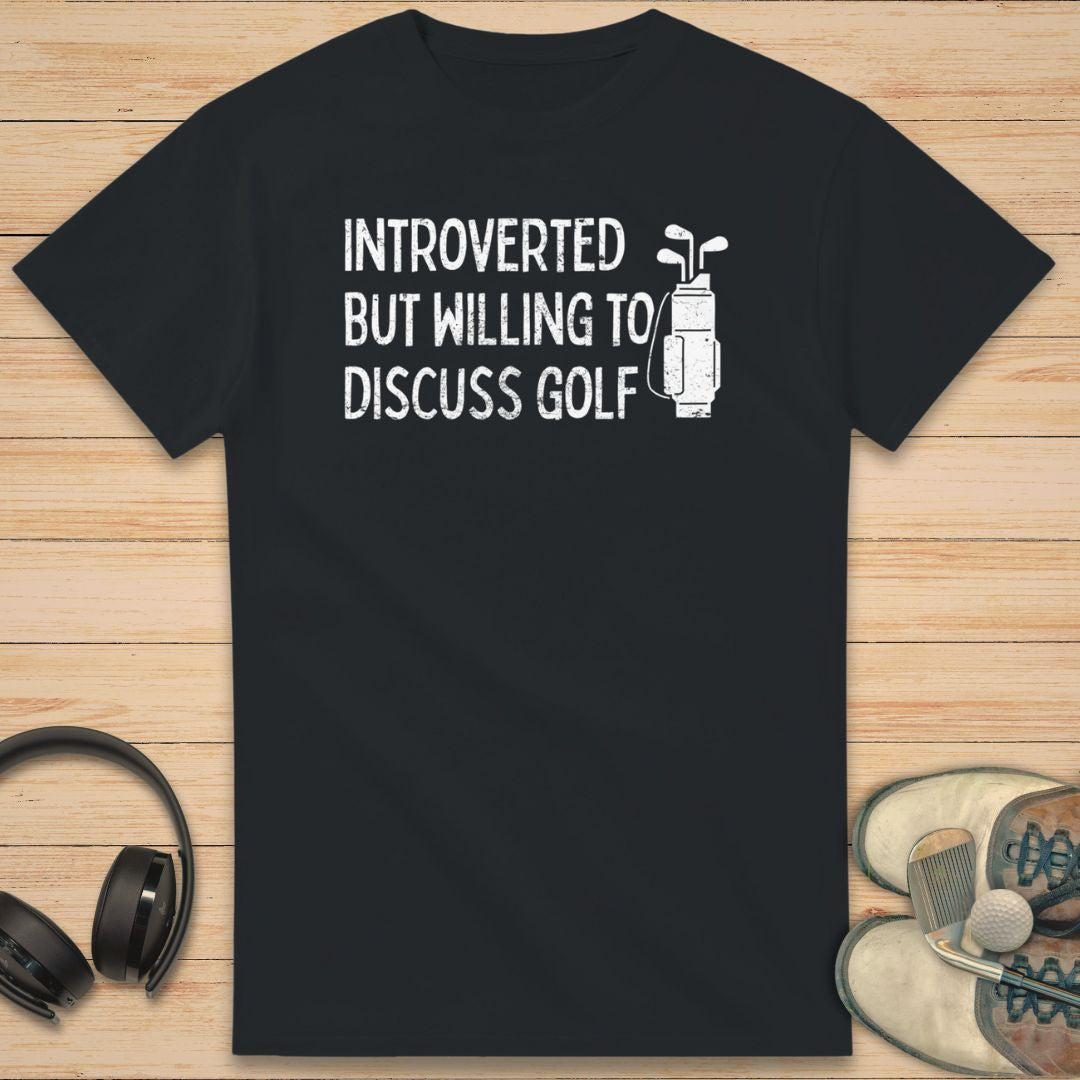 Introverted T-Shirt in Black on a light wooden floor lying next to headphones and golf shoes.