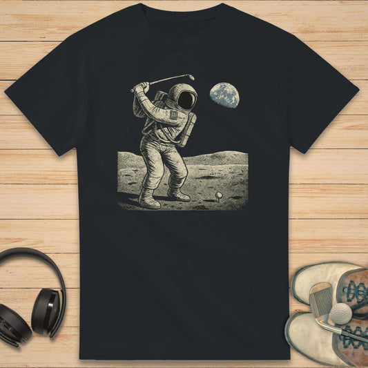 Moon Golfer T-Shirt in on a light wooden floor lying next to headphones and golf shoes.