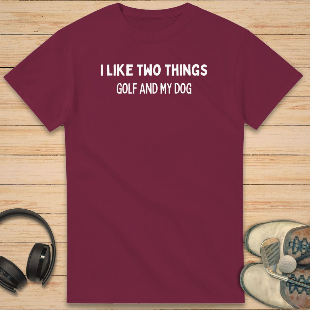 Two Things T-Shirt in Maroon on a light wooden floor lying next to headphones and golf shoes.
