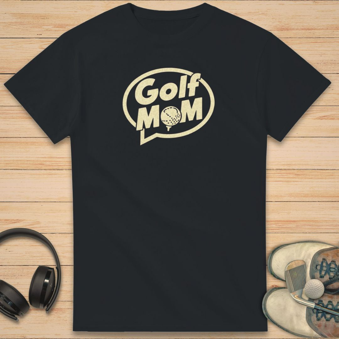 Golf Mom T-Shirt in Black on a light wooden floor lying next to headphones and golf shoes.