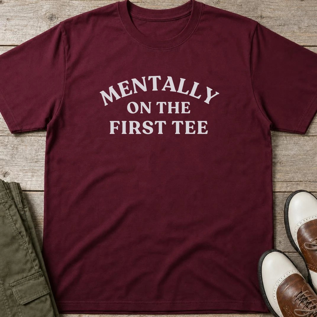 On The First Tee T-Shirt in Maroon lying on a plain floor. T-shirt is a unisex cut and 100 per cent cotton.