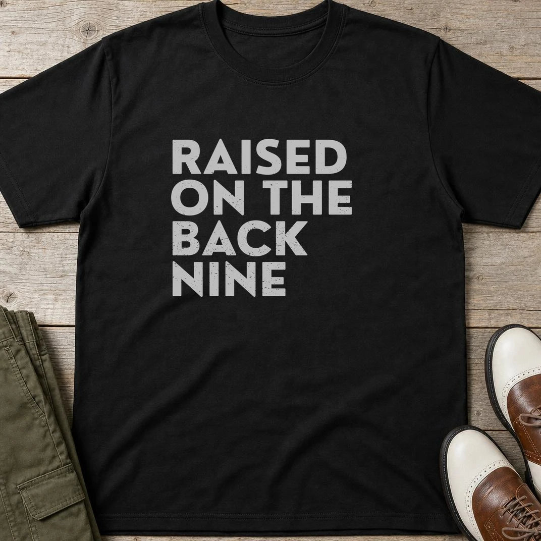 Raised On T-Shirt in Black lying on a plain floor. T-shirt is a unisex cut and 100 per cent cotton.