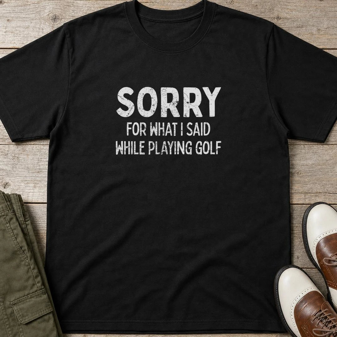 Sorry T-Shirt in Black lying on a plain floor. T-shirt is a unisex cut and 100 per cent cotton.
