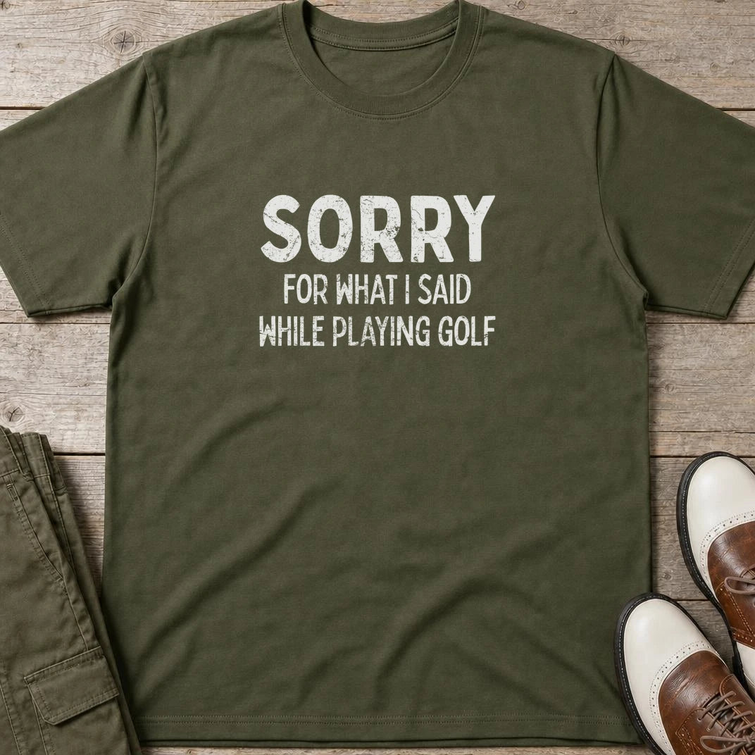 Sorry T-Shirt in Military Green lying on a plain floor. T-shirt is a unisex cut and 100 per cent cotton.