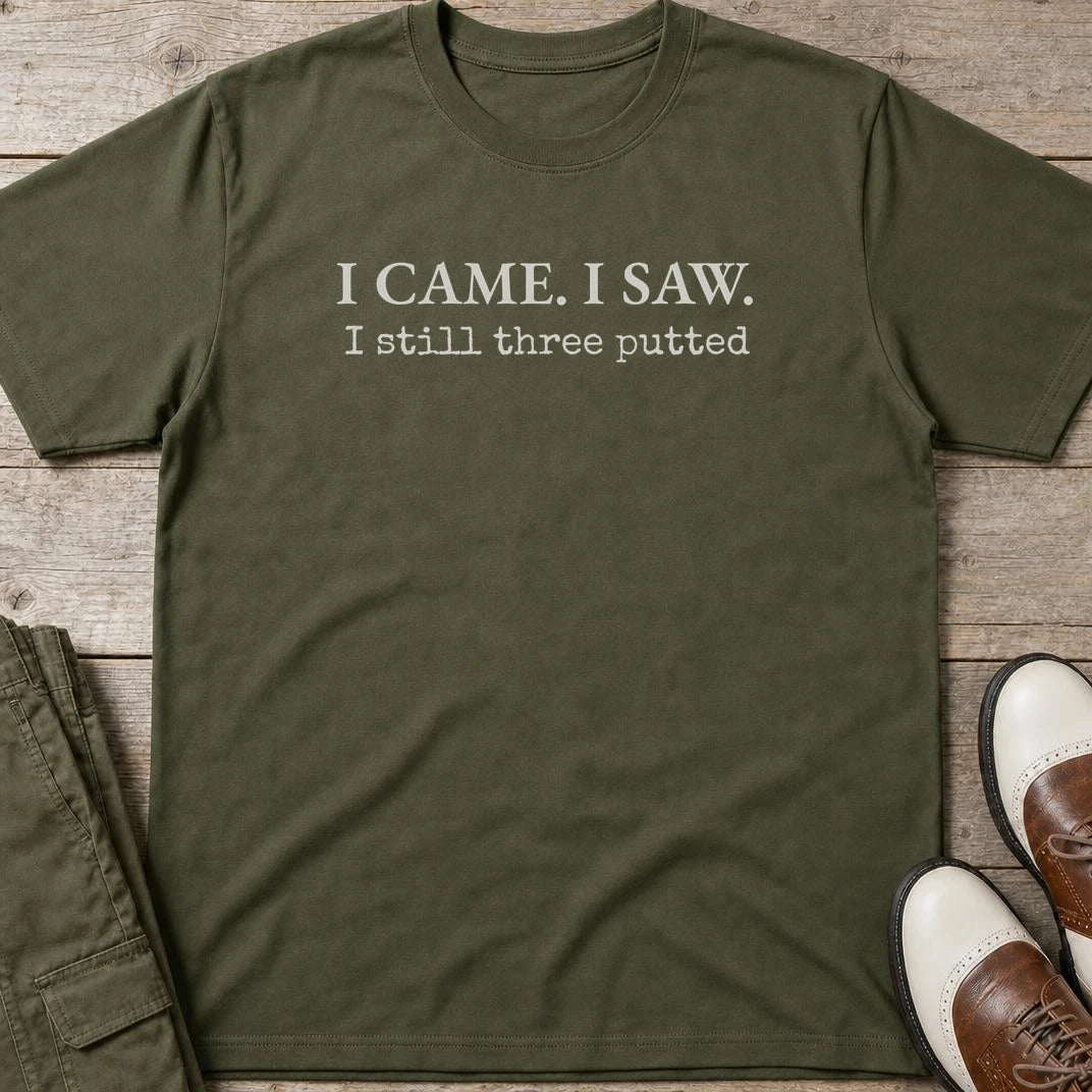 Still Three Putted T-Shirt in Military Green lying on a plain floor. T-shirt is a unisex cut and 100 per cent cotton.