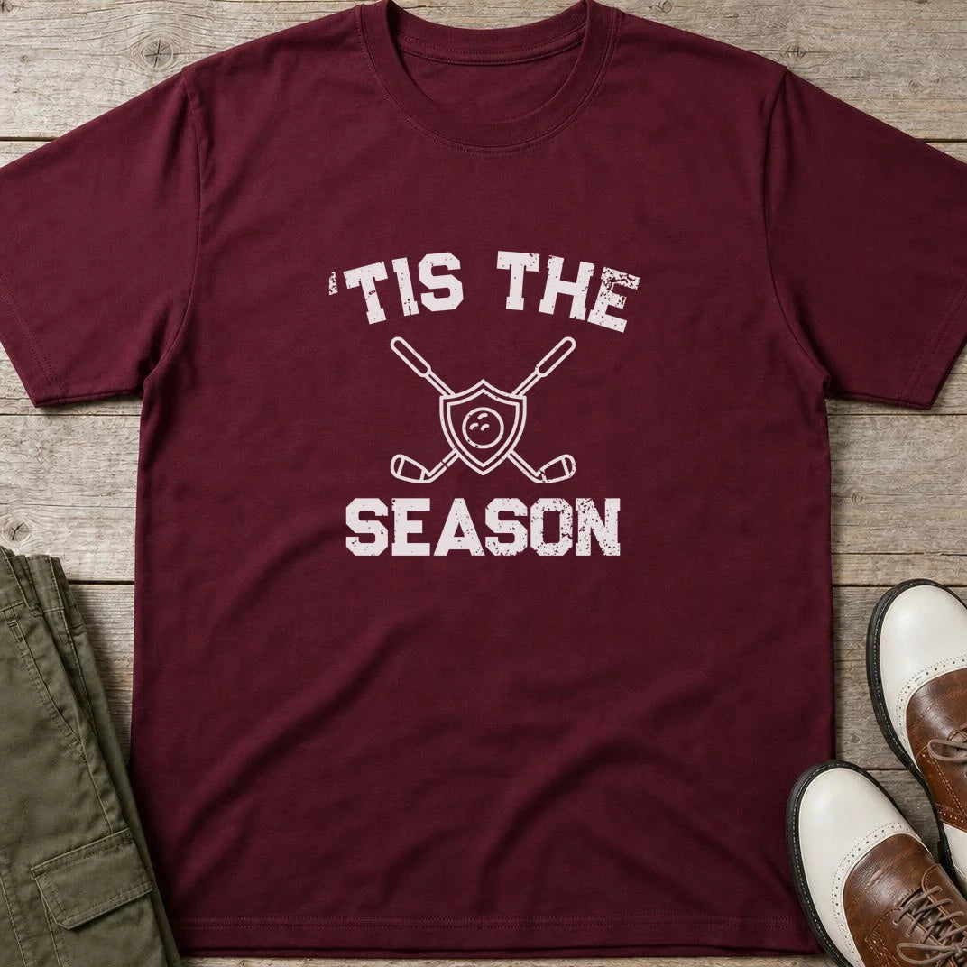 'Tis The Season T-Shirt in Maroon lying on a plain floor. T-shirt is a unisex cut and 100 per cent cotton.