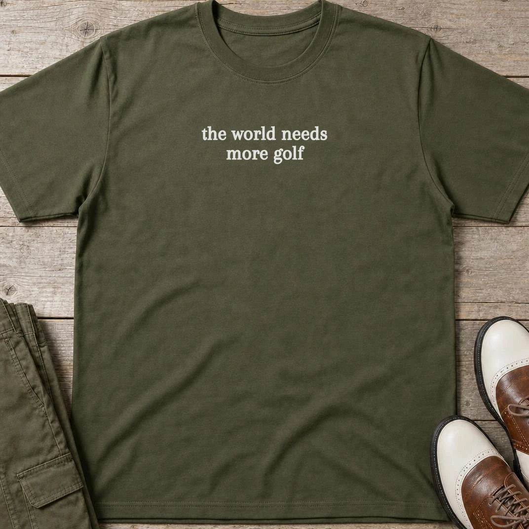 The World Needs T-Shirt in Military Green lying on a plain floor. T-shirt is a unisex cut and 100 per cent cotton.