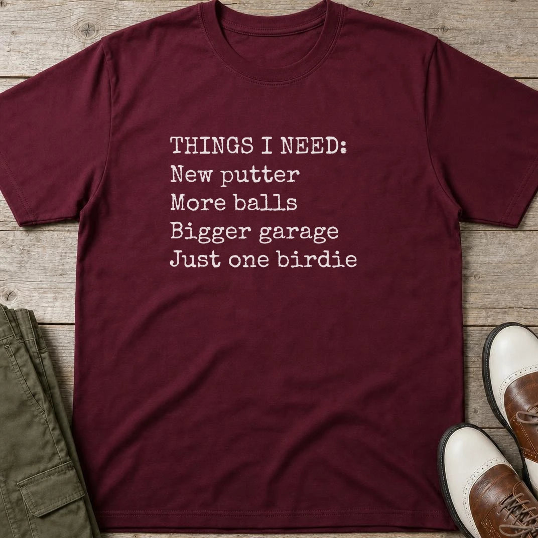 Things I Need T-Shirt in Maroon lying on a plain floor. T-shirt is a unisex cut and 100 per cent cotton.