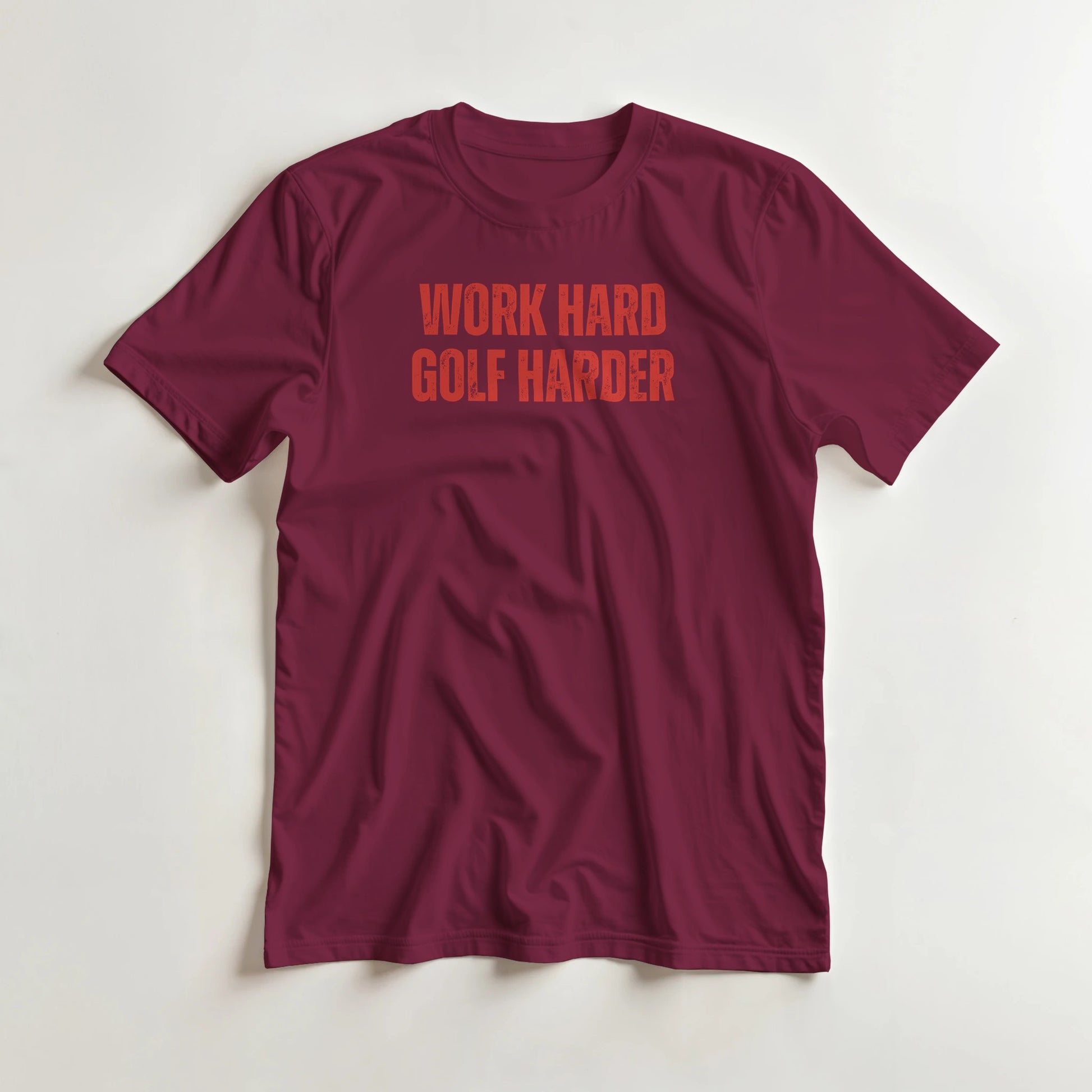 Golf Harder T-Shirt in Maroon S lying on a plain floor. T-shirt is a unisex cut and 100 per cent cotton.