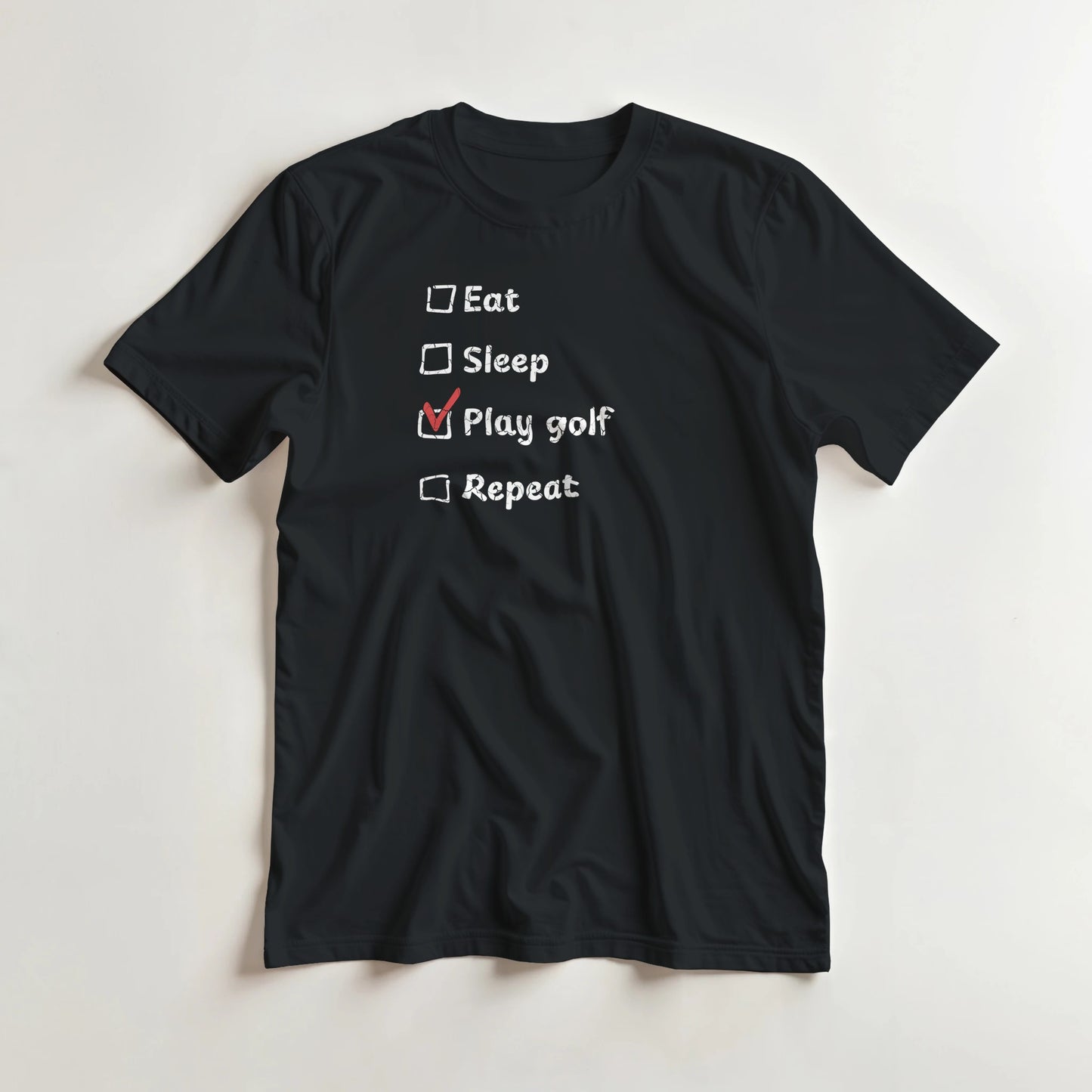 Golf Repeat T-Shirt in Black lying on a plain floor. T-shirt is a unisex cut and 100 per cent cotton.