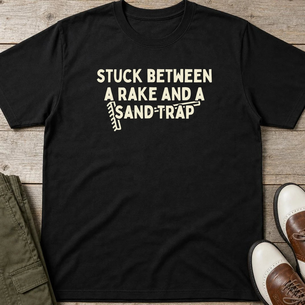 Rake Sand Trap T-Shirt in Black lying on a plain floor. T-shirt is a unisex cut and 100 per cent cotton.