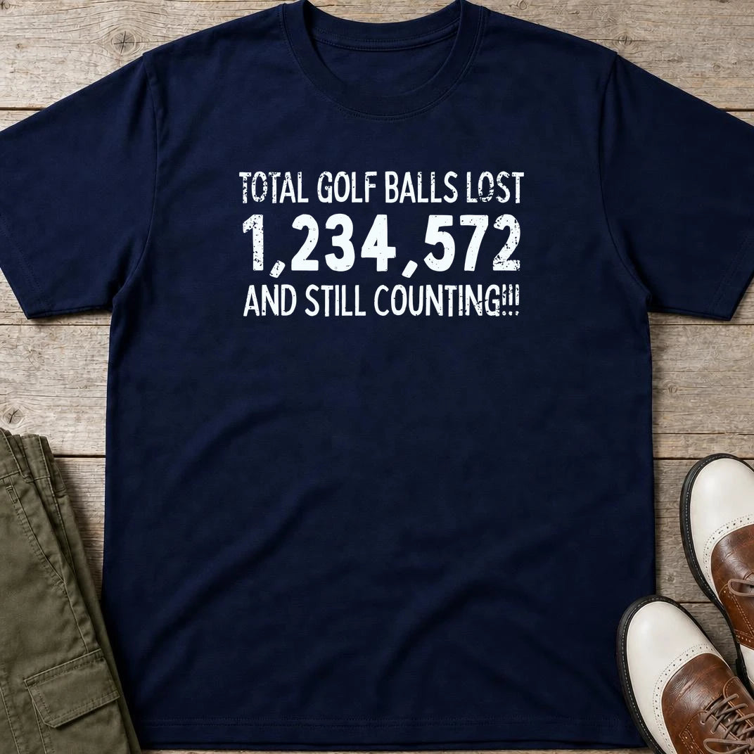 Golf Balls Lost 1,234,572 T-Shirt in Navy lying on a plain floor. T-shirt is a unisex cut and 100 per cent cotton.